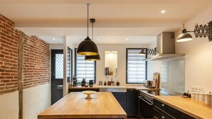 Une cuisine moderne dotée d’un îlot central, de luminaires suspendus noirs et d’un mur d’accent en briques.