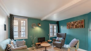 Un salon chaleureux avec des murs de couleur turquoise, un canapé, un fauteuil, une petite table ronde et un téléviseur.