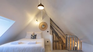 Une chambre avec un grand lit, un luminaire suspendu, un miroir rond et un escalier en bois.