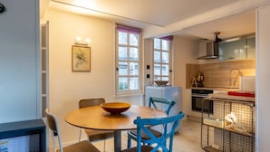 Une cuisine compacte avec un coin repas, comprenant une table ronde, des chaises bleues et un saladier posé sur la table.