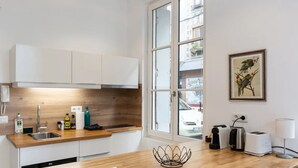 Une cuisine moderne avec des meubles blancs, un plan de travail en bois, un évier et une fenêtre donnant sur la rue.