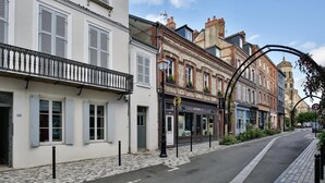 Une rue bordée d’immeubles, un trottoir pavé et un ciel dégagé.