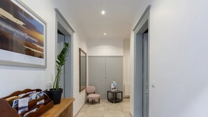 Un couloir avec un banc en bois, une plante en pot, un tableau encadré, une chaise et une petite table sur laquelle se trouve un magazine.