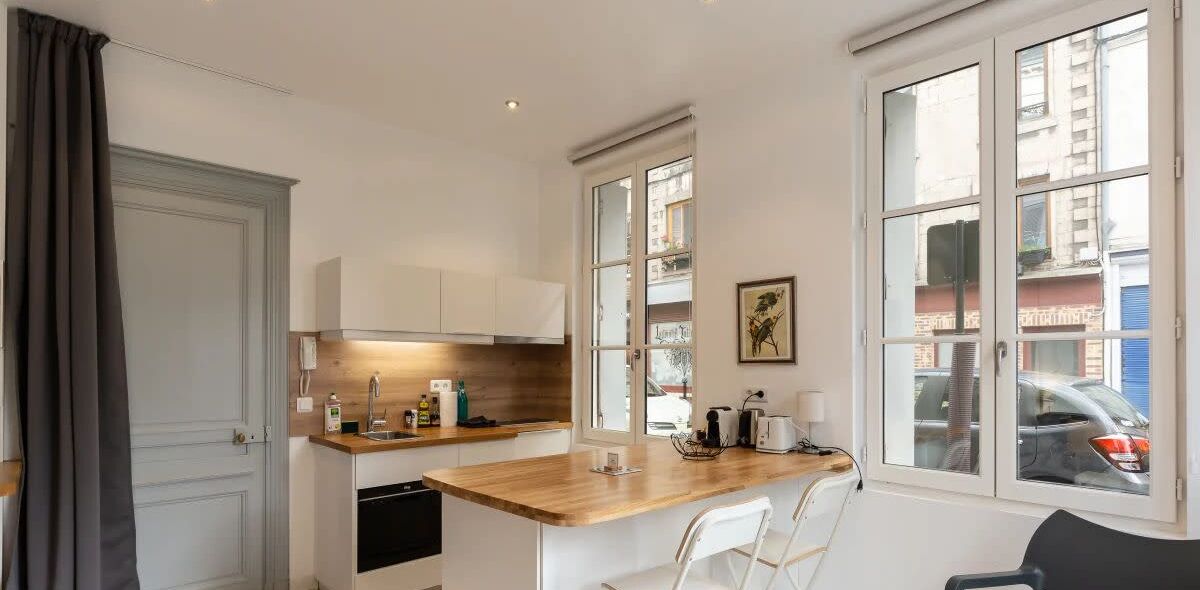 A compact kitchen with a wooden countertop, white cabinets, and a window with a view of the street.