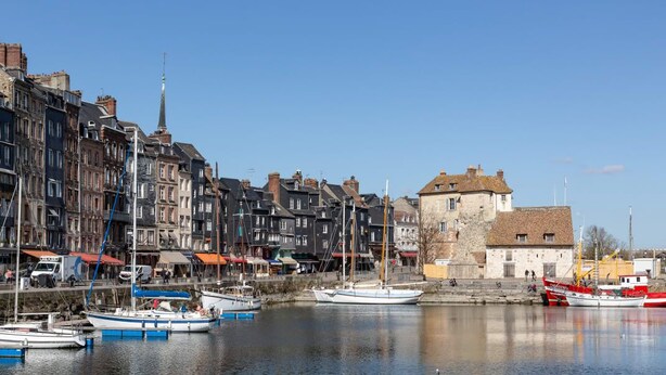 A harbor with boats docked, a historic building, and a church spire.