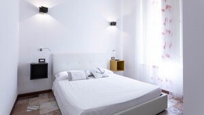 Una camera da letto con un letto grande, due lampade a parete, una piccola mensola e una finestra con tende leggere.