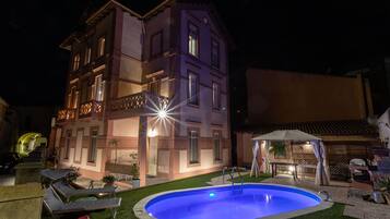 A multi-story building with a swimming pool, outdoor seating, and a well-lit facade.
