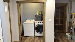 A laundry room with a washing machine and dryer, wooden flooring, and a door leading to another room.