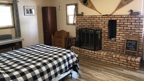 A room with a checkered bed, a fireplace, a ceiling fan, and a wooden cabinet.