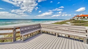 A wooden deck with benches overlooking a beach and ocean.