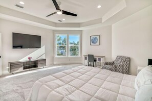 A bedroom with a large bed, a desk, a chair, a TV mounted on the wall, and a window with a view of trees. - Serenity Starts at White Sands Retreat / Steps to Resort Community Pool / 4 Bikes (Santa Rosa Beach)