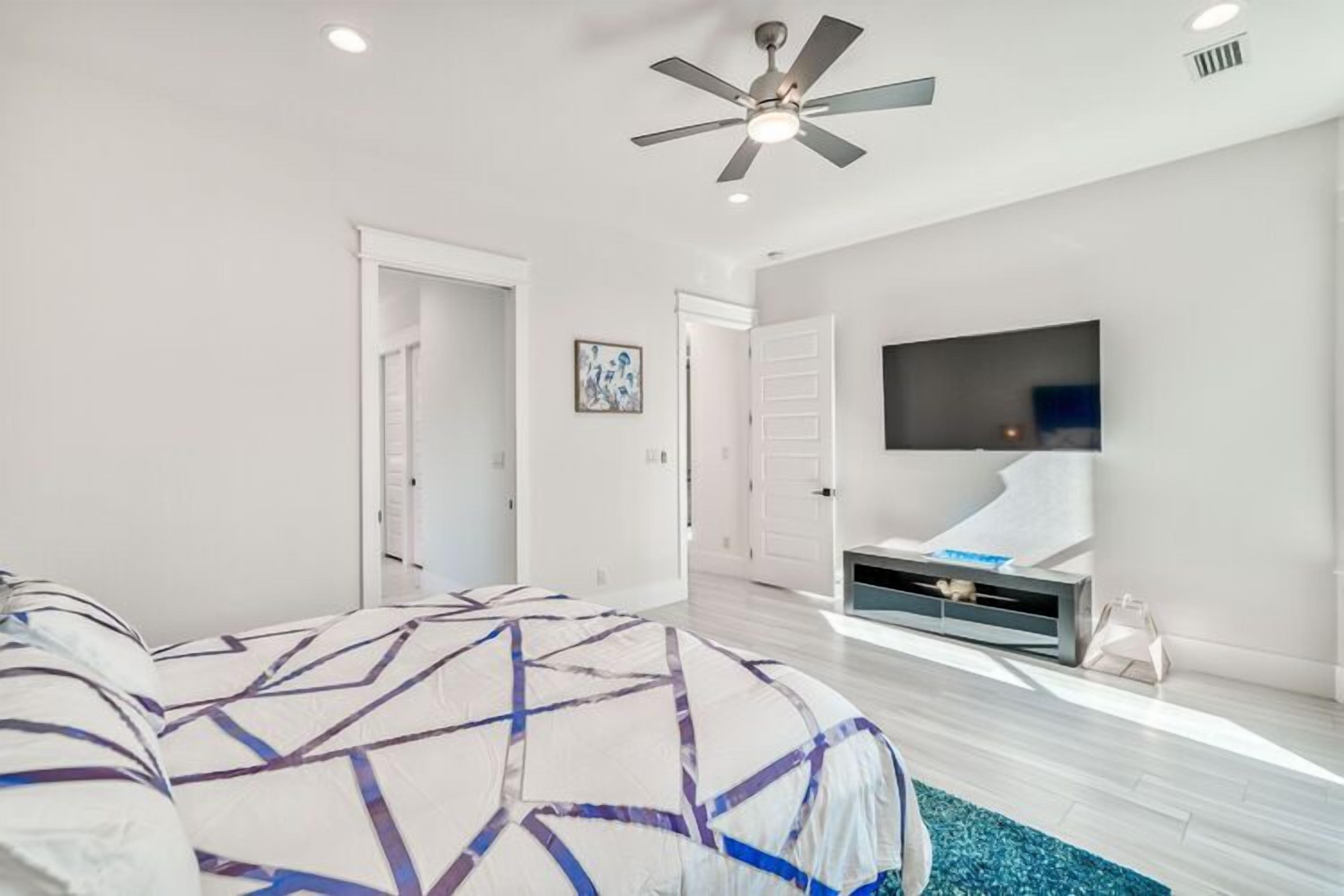 A bedroom with a bed, a ceiling fan, a TV, and a walk-in closet.