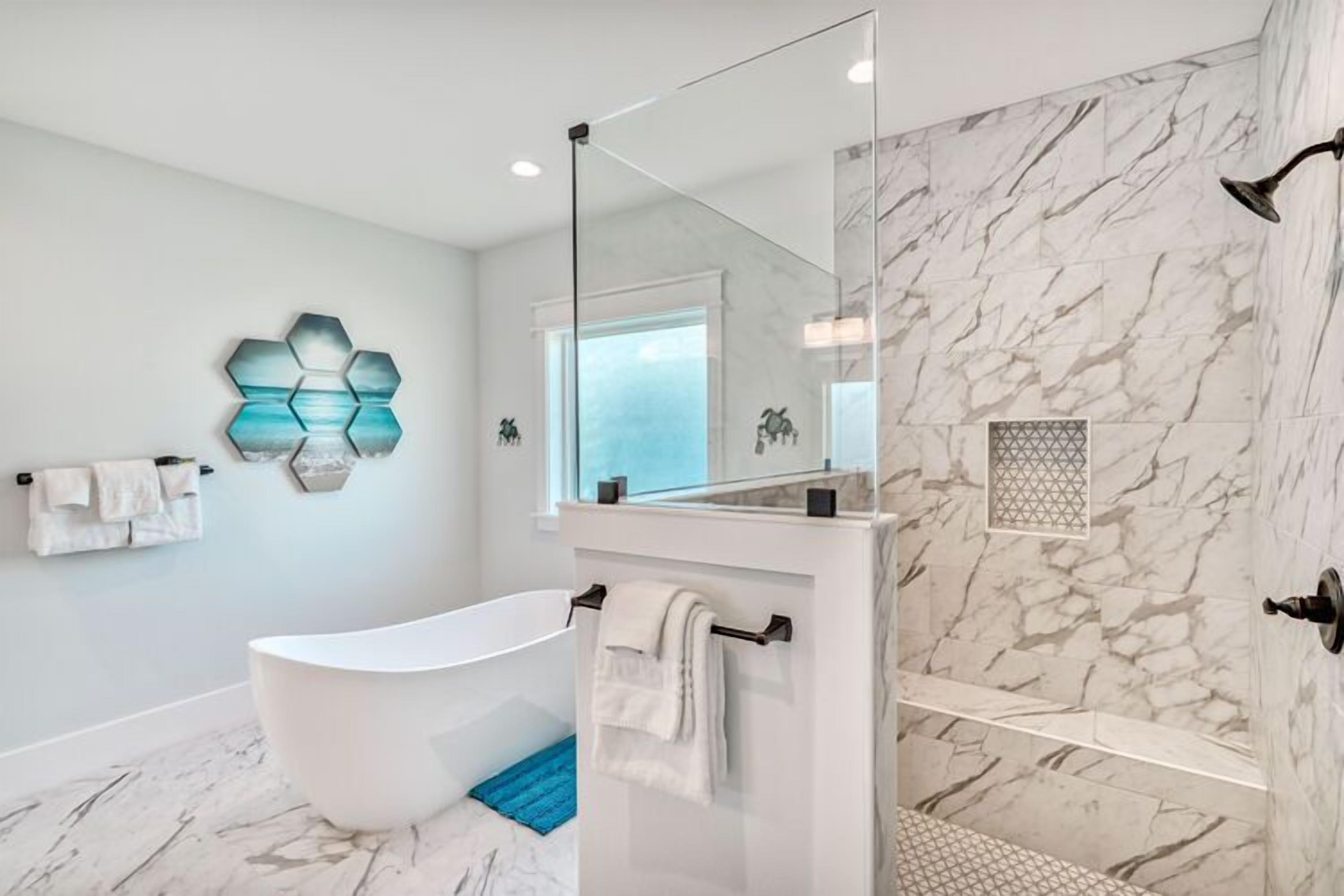 A modern bathroom with a freestanding bathtub, a glass shower enclosure, marble walls, and a geometric wall art piece.