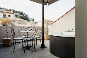 A balcony with a hot tub, two chairs, and a potted plant. - Espero Royal Stay (Nafplio)