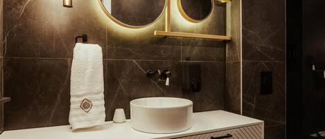 Un baño moderno con un espejo grande, un espejo redondo, un lavabo blanco y un inodoro.