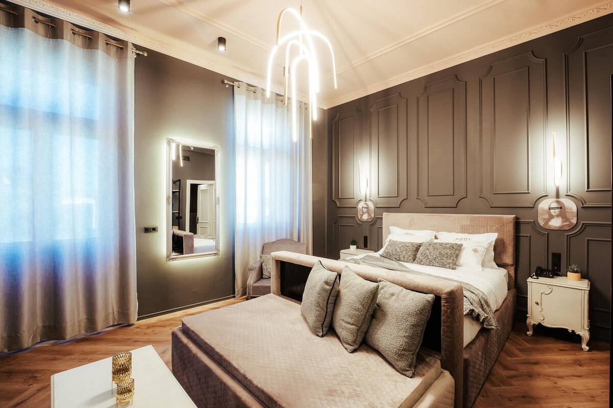 A bedroom with a large bed, a bedside table, a nightstand, a mirror, and a chandelier.