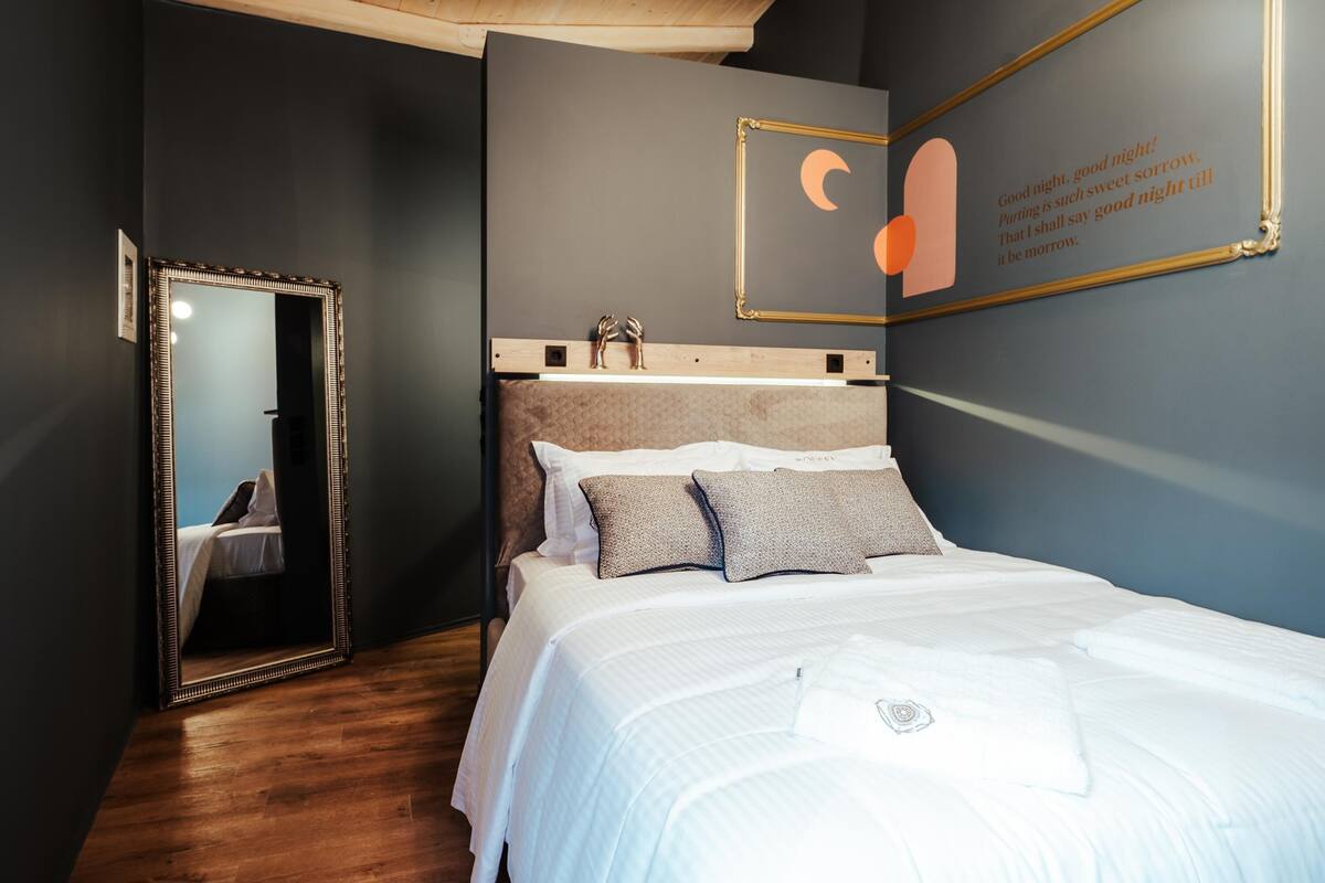 A bedroom with a large mirror, a bed with white bedding, and a wall with a framed quote.