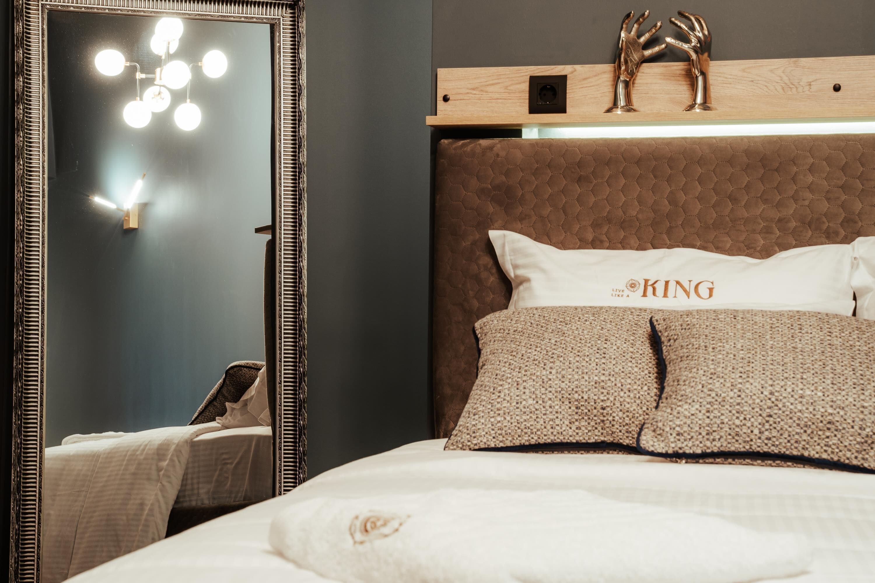 A neatly made bed with a headboard, a mirror with lights, and a decorative item on the headboard.