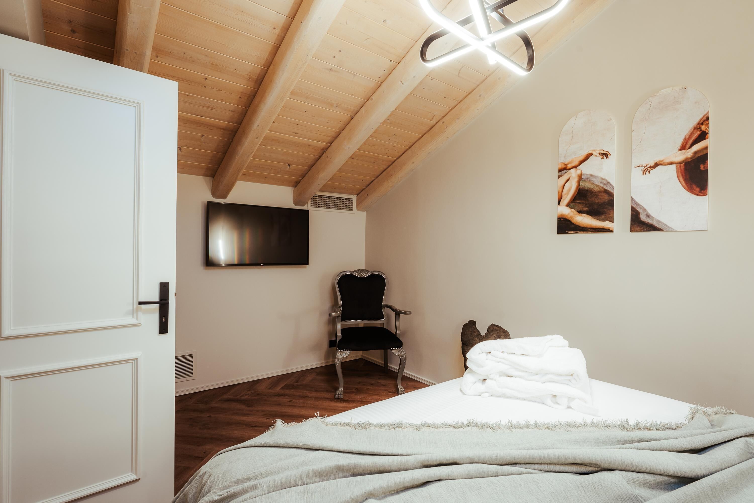 A bedroom with a bed, a chair, a TV, and wooden ceiling beams.
