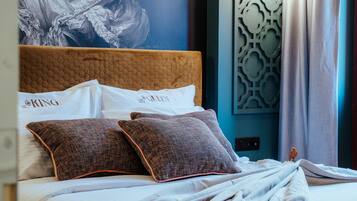 A neatly made bed with a brown headboard and two patterned pillows, a large abstract painting on the wall, and a decorative wall panel.