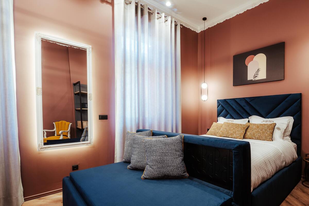 A bedroom with a bed, a mirror, a chair, and a wall-mounted artwork.