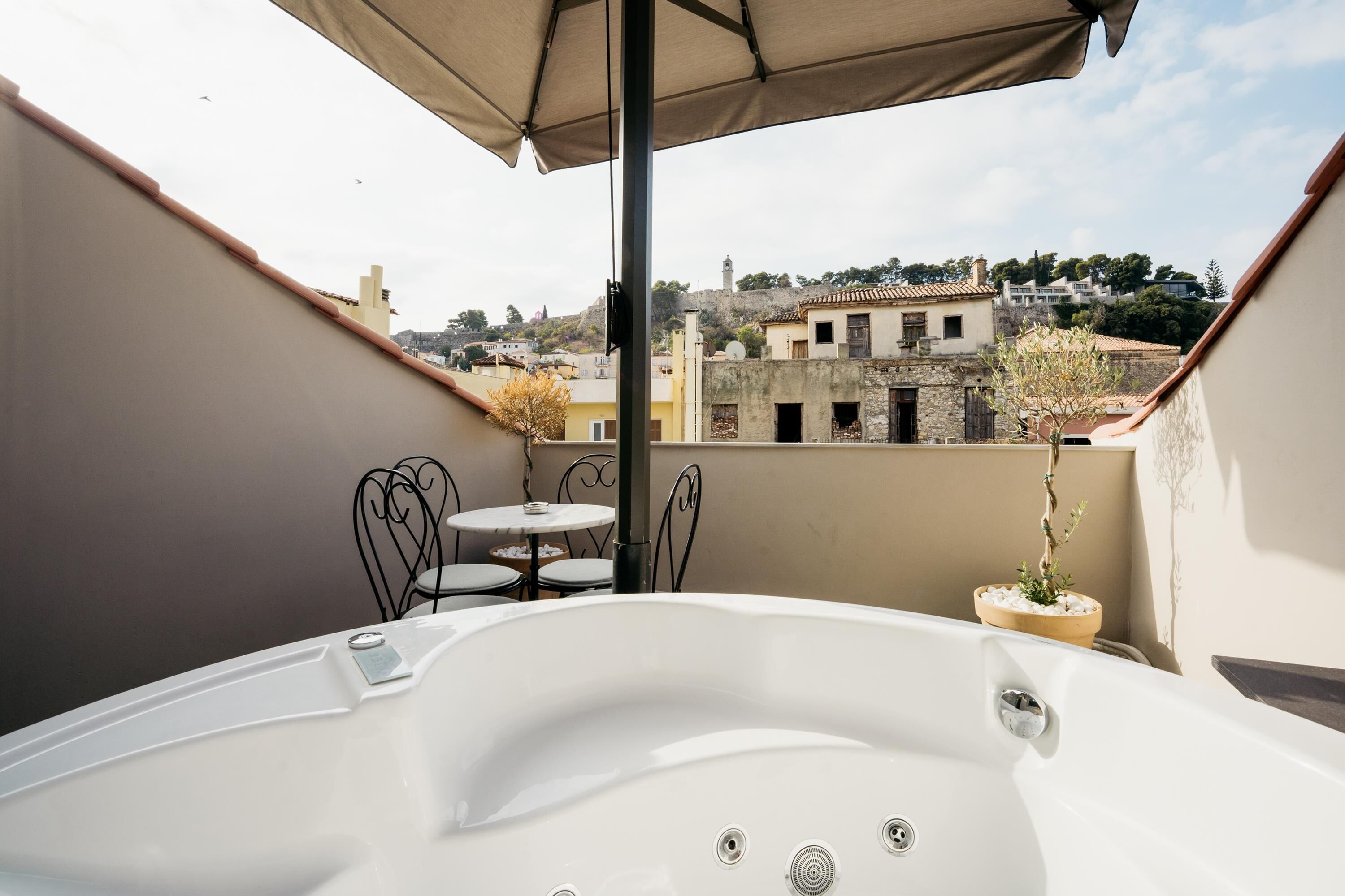 Una terraza en la azotea con un jacuzzi, una mesa y sillas, con vistas a un paisaje urbano.