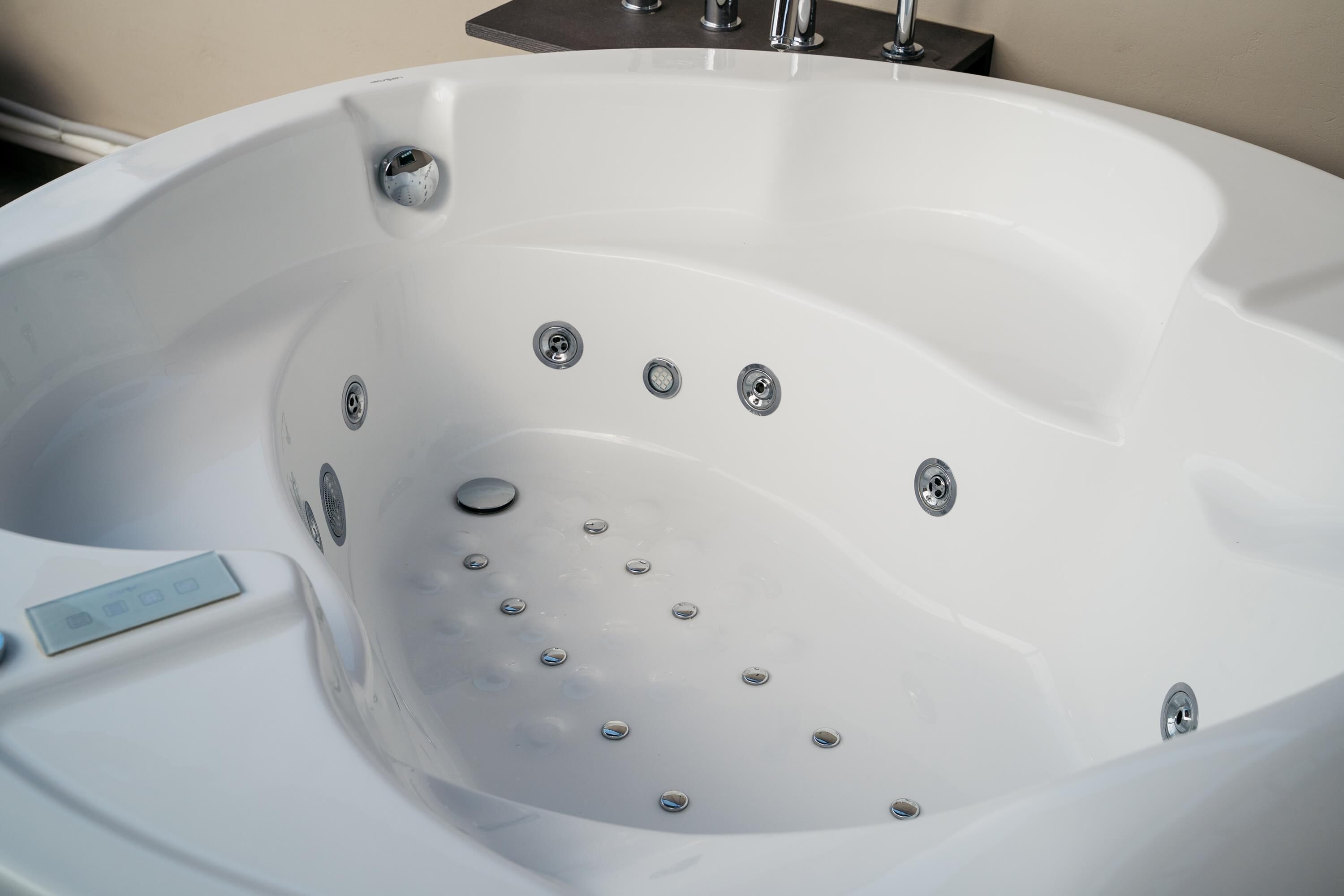 A white hot tub with multiple jets, a control panel, and a drain plug.