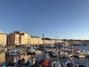 Satamassa on laivoja, jotka on ankkuroitu laiturin viereen, ja rannan varrella on rakennuksia. Taivas on kirkas.