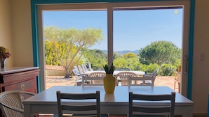 A dining area with a table and chairs, a vase with flowers, and a view of the outdoors.