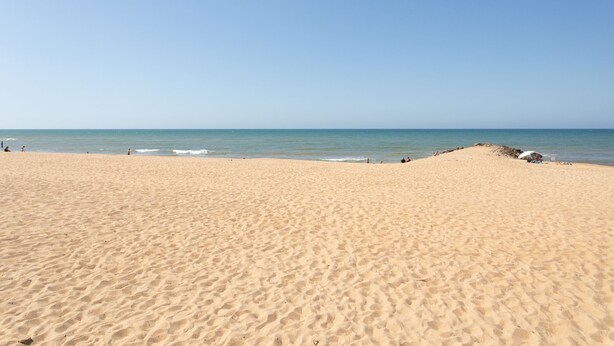 Une vaste plage de sable fin, avec un ciel dégagé et une mer calme.