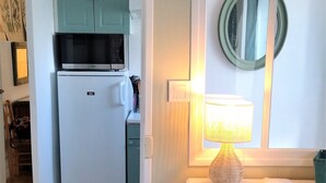 A compact kitchen with a refrigerator, microwave, and teal cabinets. A small table with a lamp and a magazine is visible. - "Un Petit Coin de Paradis" (Saint-Nazaire)