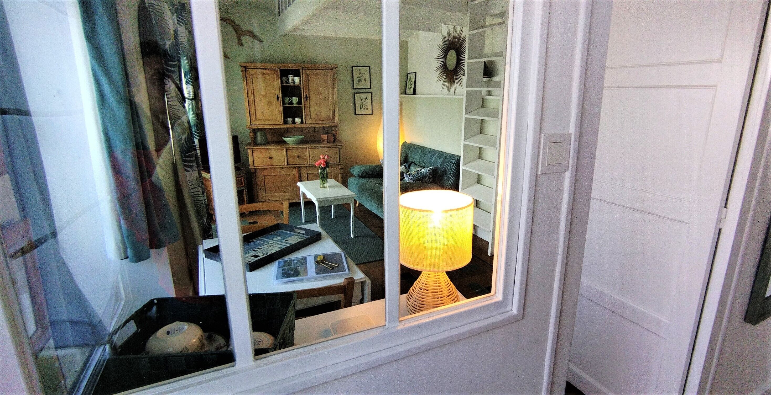 Ein Zimmer mit Fenster, einem Tisch mit Lampe, einem Stuhl, einer Couch und einem Schrank.