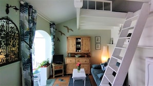 A cozy living room with a sofa, a coffee table, and a TV. There's a wooden cabinet with decorative items and a staircase. - "Un Petit Coin de Paradis" (Saint-Nazaire)