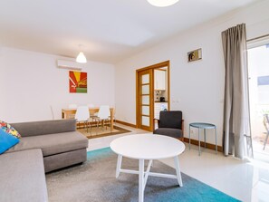 A modern living room with a grey sofa, a round white table, and a dining area with white chairs.