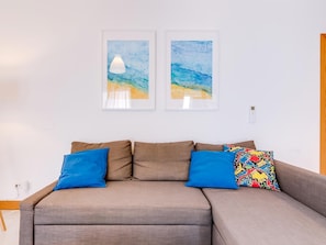 A modern living room with a grey sectional sofa, two framed abstract paintings, and a colorful throw pillow.