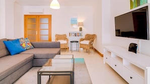 Ein modernes Wohnzimmer mit einer Couch, einem Glastisch, einem Fernseher und einem Bücherregal.