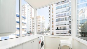 Una cocina moderna con lavadora integrada, encimera blanca y un amplio ventanal con vistas a rascacielos.
