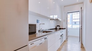Una cocina moderna con armarios blancos, un lavamanos de acero inoxidable y un horno empotrado.