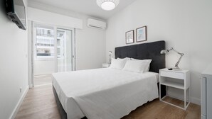 Un dormitorio moderno con una cama grande, una mesita de noche con lámpara y vistas al balcón exterior.