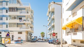 Vista de la calle con edificios de varios pisos, coches estacionados y cielo despejado.