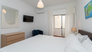 Ein Schlafzimmer mit einem Bett, einem Fernseher, einer Kommode, einem Sessel und einem Bild an der Wand.