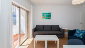 Ein modernes Wohnzimmer mit einem grauen Sofa, einem weißen Couchtisch und einem blauen Sessel. Ein großes Fenster bietet Blick auf ein Gebäude.