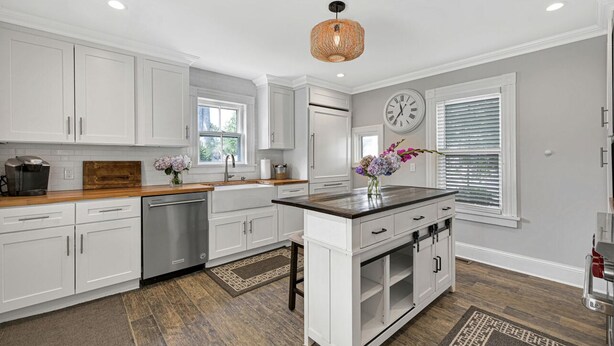 Una cocina moderna con armarios blancos, encimera de madera, una isla integrada y una lámpara colgante.