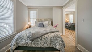 Un dormitorio con una cama grande, una mesita de noche y una lámpara. Hay una puerta que conduce a otra habitación.