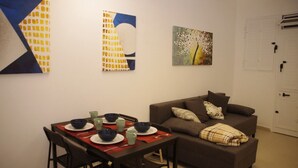 Un coin repas avec une table dressée pour quatre personnes, un canapé marron avec des coussins et des œuvres d’art abstraites accrochées au mur.