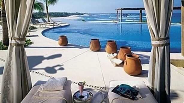 Un salon au bord de la piscine offrant une vue sur l’océan, avec des chaises longues et des pots en terre cuite.