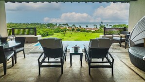 Un espace extérieur aménagé, abrité et doté de deux chaises et d’une table, offrant une vue sur un paysage verdoyant et luxuriant ainsi que sur l’océan.