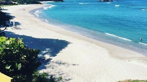 Une plage avec une eau turquoise et limpide, un rivage sablonneux et quelques zones verdoyantes en arrière-plan.