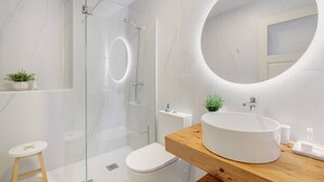 Une salle de bain moderne avec une douche à parois de verre, un miroir rond, un meuble-lavabo en bois et un lavabo blanc.