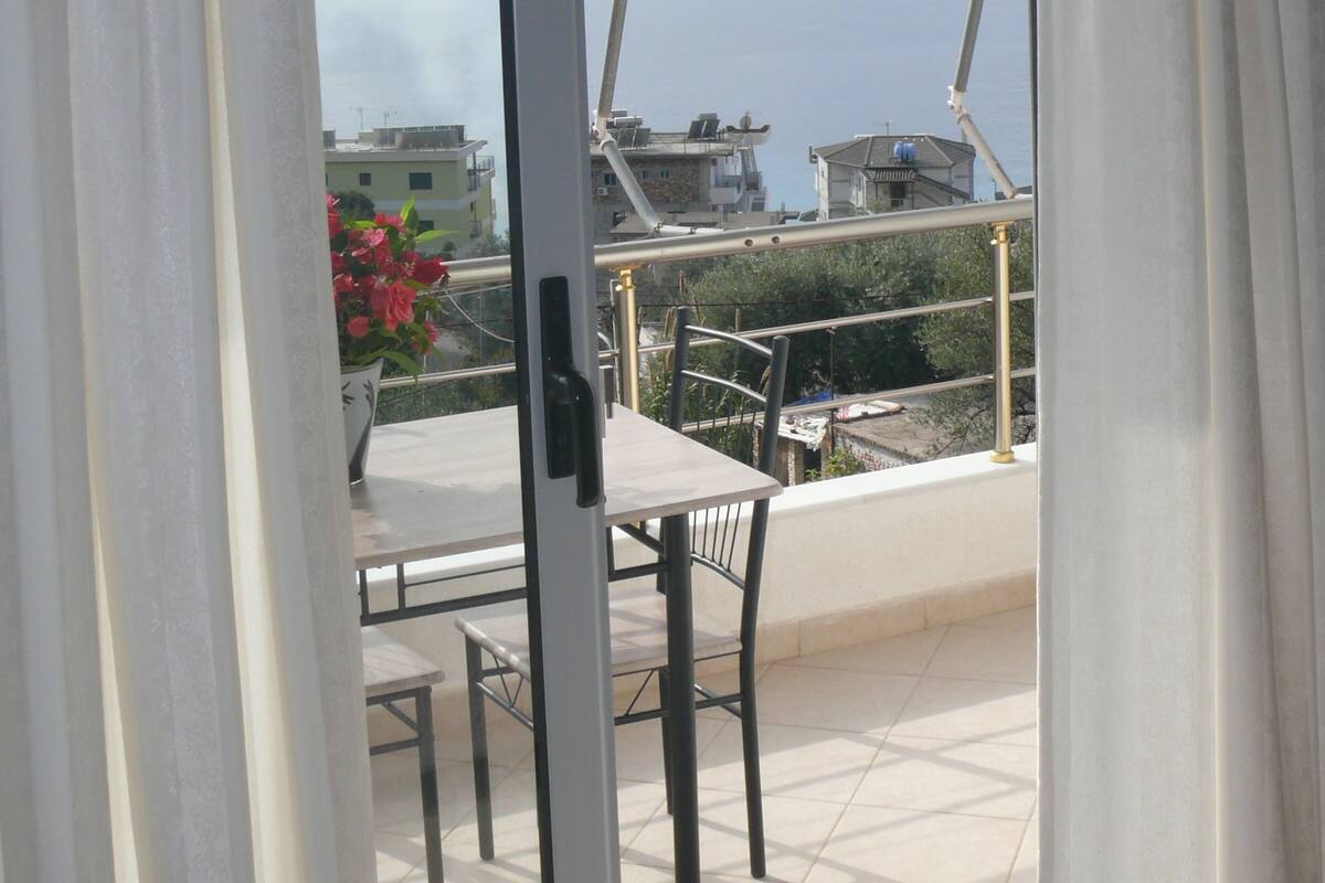 Un balcón con una mesa y sillas, con vista a un cuerpo de agua y edificios.